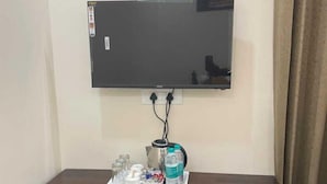 Ein Flachbildfernseher ist an der Wand über einem Holzschrank montiert, auf dem ein Tablett mit einer Wasserflasche, Gläsern und einer kleinen Schale steht.