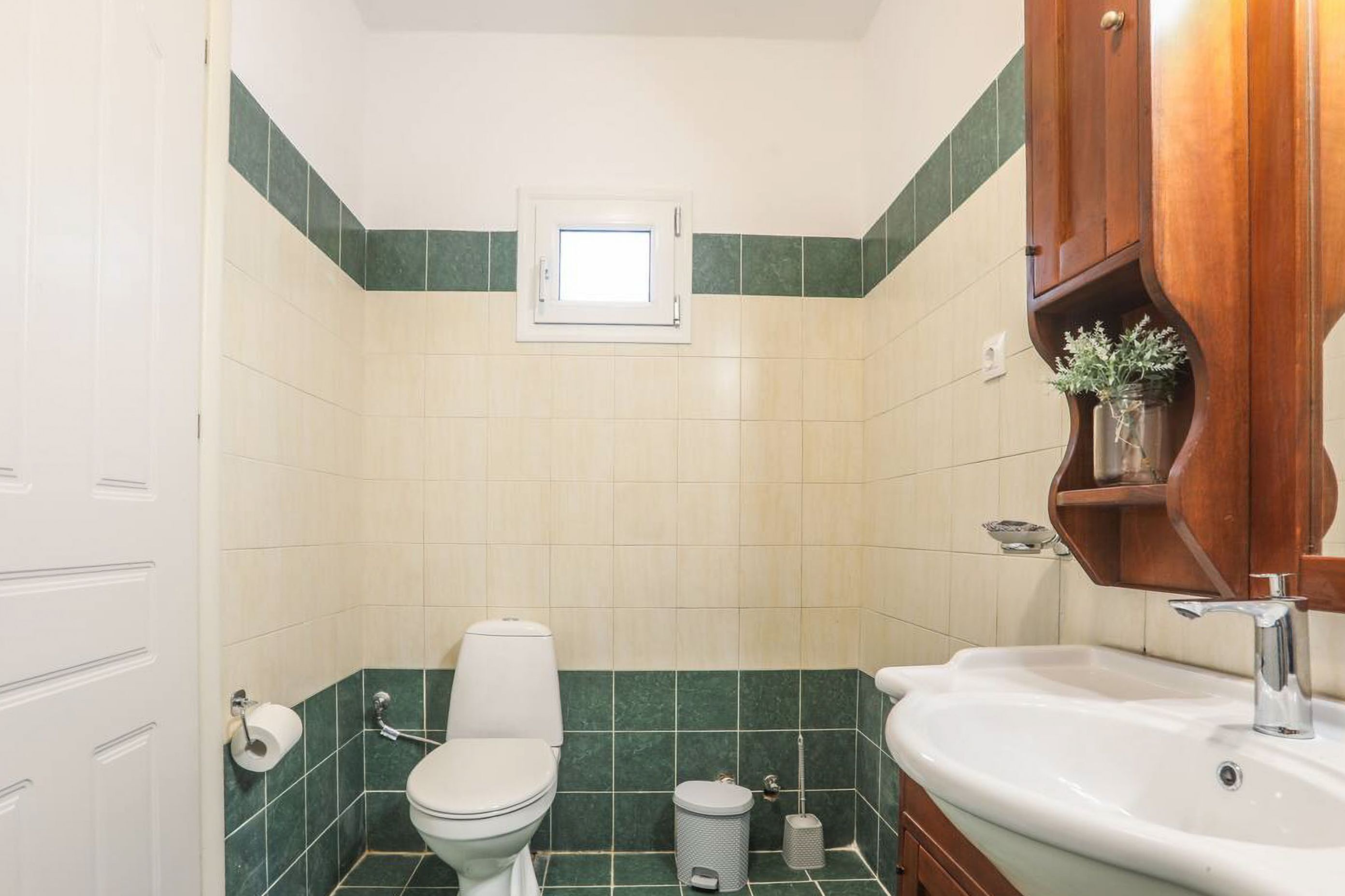 Un baño con inodoro, lavamanos y un ventanal pequeño.