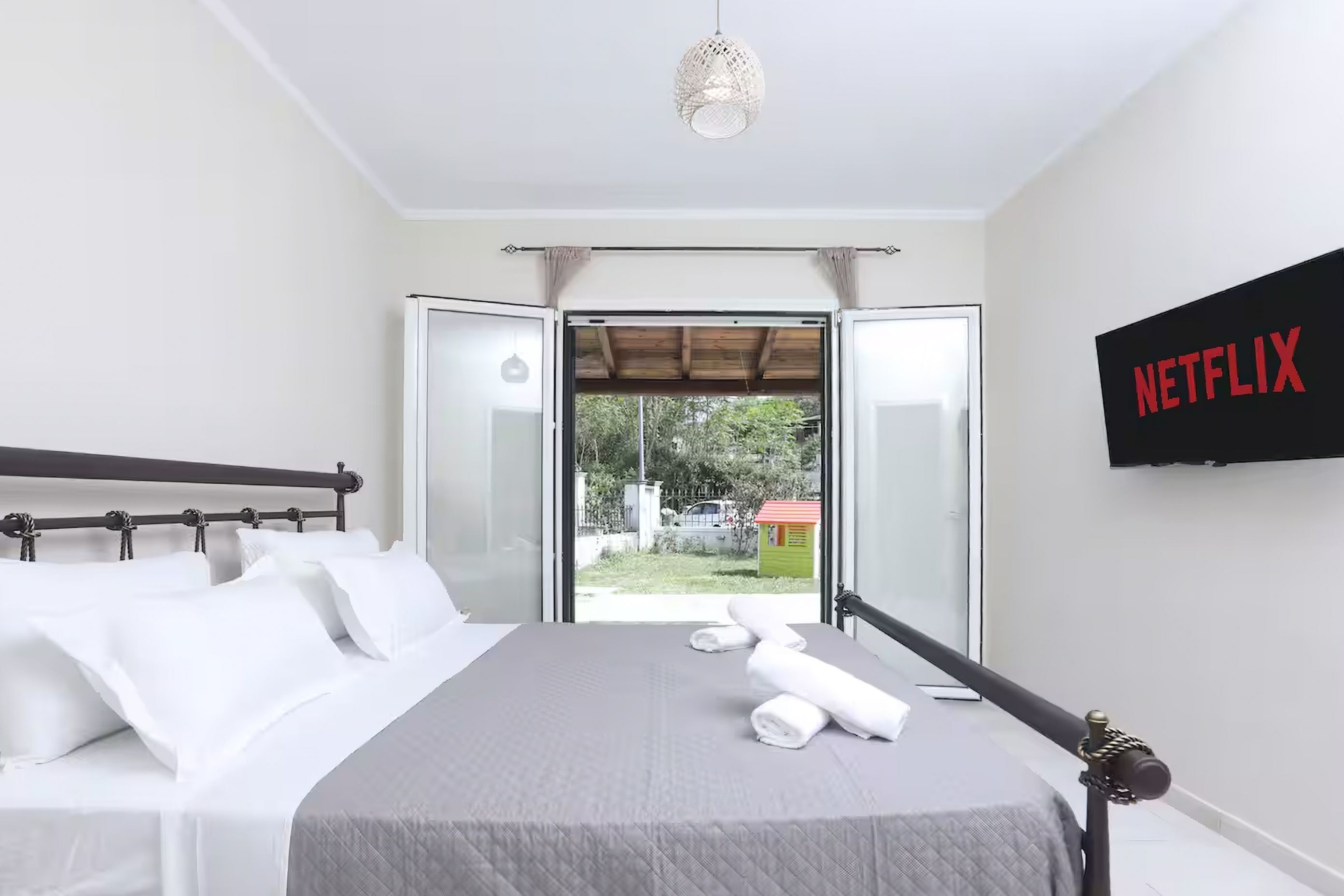 A bedroom with a bed, a TV mounted on the wall, and a sliding glass door leading to an outdoor area.
