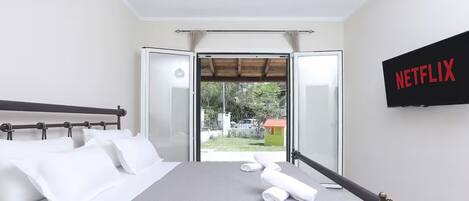 A bedroom with a bed, a TV mounted on the wall, and a sliding glass door leading to an outdoor area.