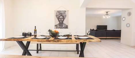 Uma sala de jantar com mesa de madeira posta para quatro pessoas, uma fruteira e uma obra de arte pendurada na parede.