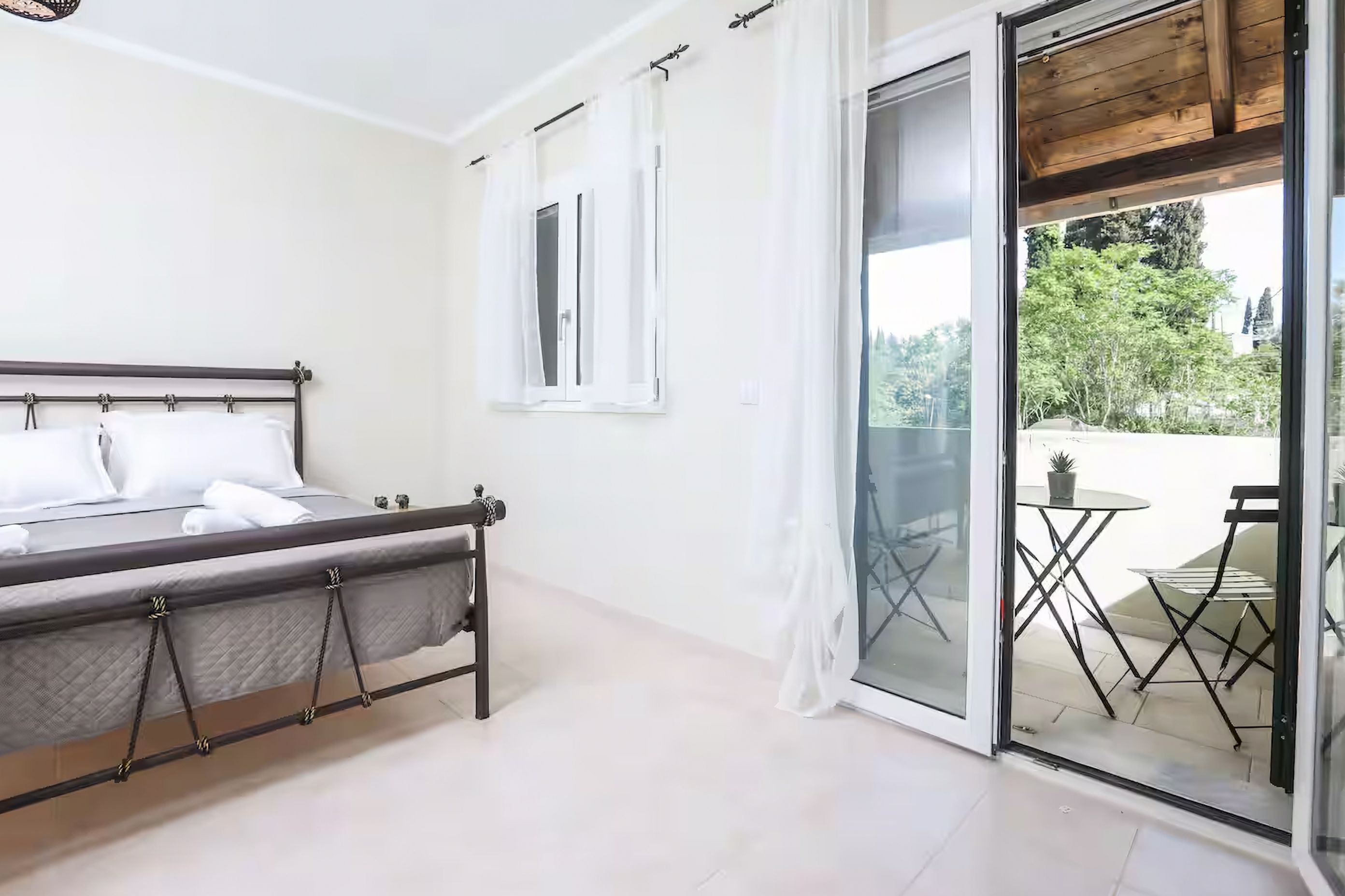 Quarto com cama, janela e porta de vidro deslizante para área externa com mesa e cadeiras.