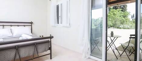 Quarto com cama, janela e porta de vidro deslizante para área externa com mesa e cadeiras.