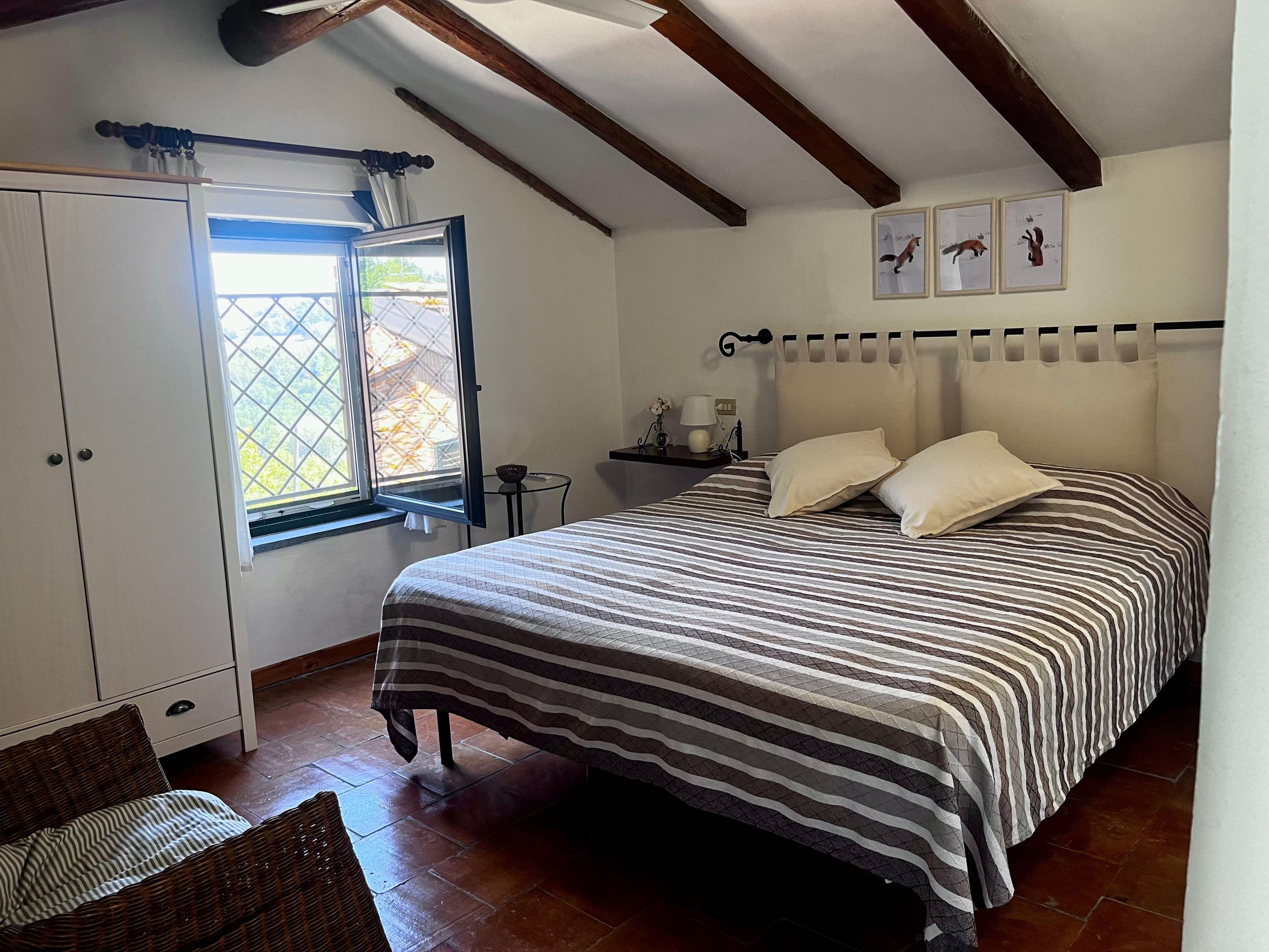 Une chambre à coucher avec un lit, une fenêtre, une armoire et une petite table avec une lampe.
