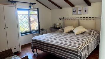 Une chambre à coucher avec un lit, une fenêtre, une armoire et une petite table avec une lampe.