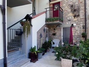 A multi-level outdoor area with steps, potted plants, a white chair, and a red door.