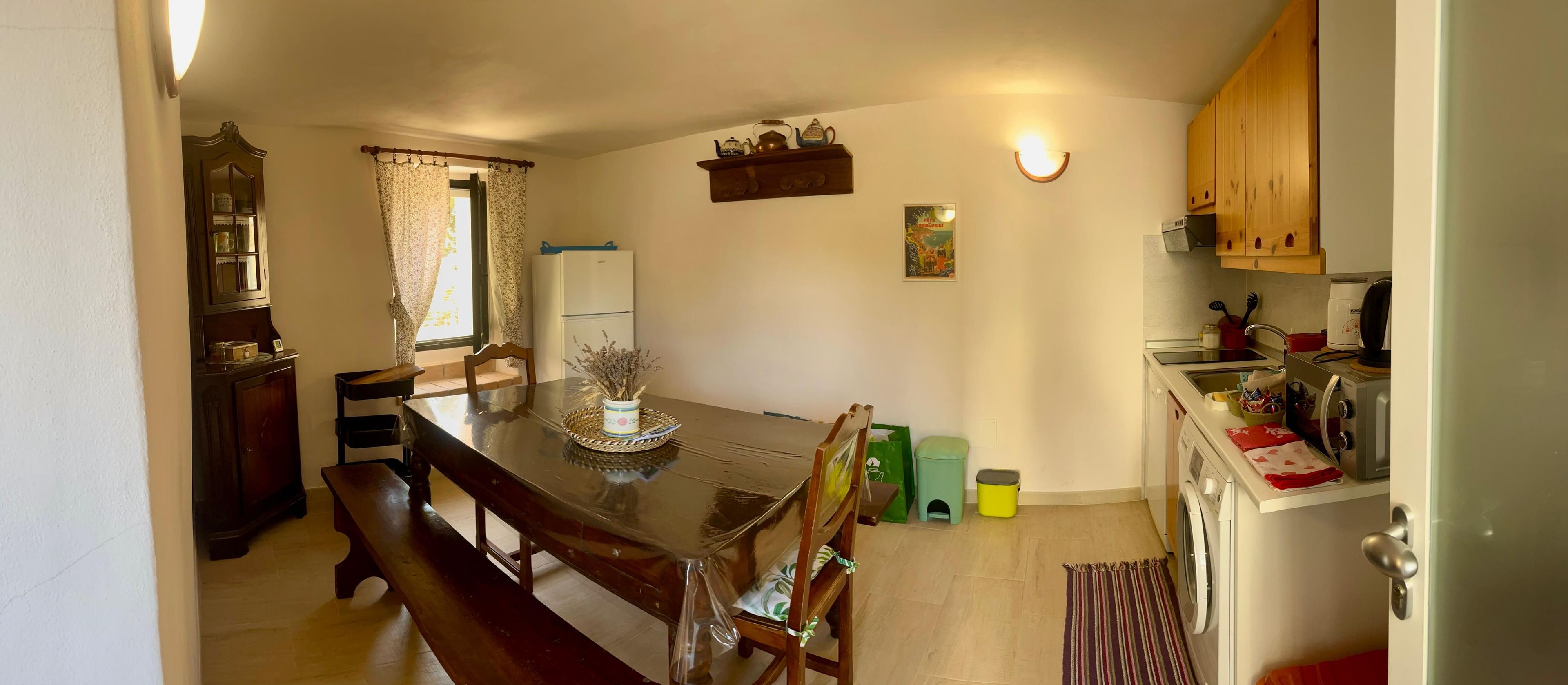 Zona pranzo con tavolo in legno, sedie, frigorifero, forno a microonde e lavatrice.