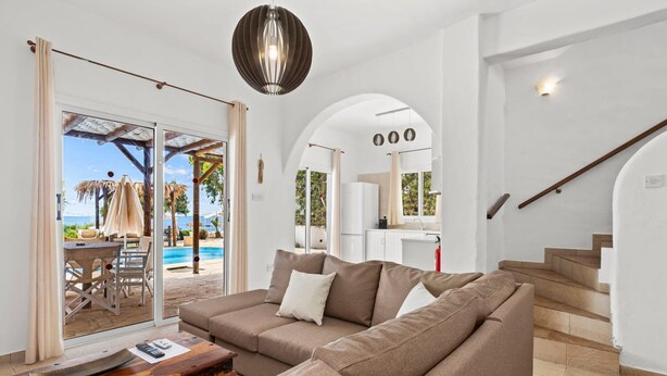 Un soggiorno moderno con un divano componibile, un tavolino in legno e una porta vetrata che dà su una zona piscina.