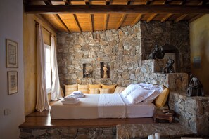 A bedroom with a stone wall, wooden beams, a bed with white linens, and a small statue on a shelf. - Topos exclusive Mykonos- Villa Poseidon (Agios Ioannis Diakoftis)
