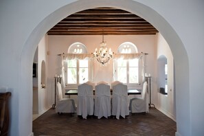 A dining area with a high arched ceiling, a chandelier, and a table set for six with white chairs. - Topos exclusive Mykonos- Villa Poseidon (Agios Ioannis Diakoftis)