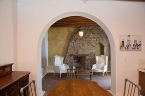 A cozy room with a stone fireplace, white armchairs, and a wooden table. - Topos exclusive Mykonos- Villa Poseidon (Agios Ioannis Diakoftis)