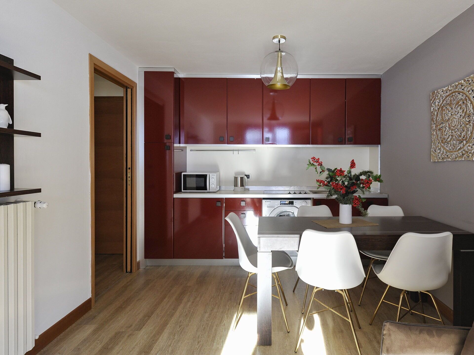 A compact kitchen with red cabinets, a microwave, a sink, and a dining area with a table and chairs.