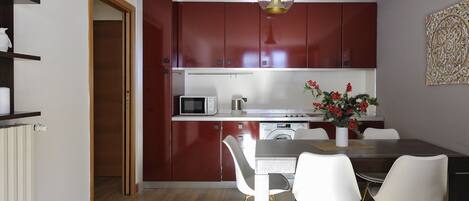 A compact kitchen with red cabinets, a microwave, a sink, and a dining area with a table and chairs.