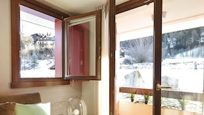 A room with a sofa, a clear glass table, a red cabinet, and a balcony with a view of a snowy landscape. - Residenze Holiday Park by Halldis (Ponte di Legno)