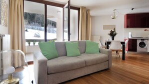 A living room with a sofa, a dining area, a washing machine, and a view of a snowy landscape. - Residenze Holiday Park by Halldis (Ponte di Legno)