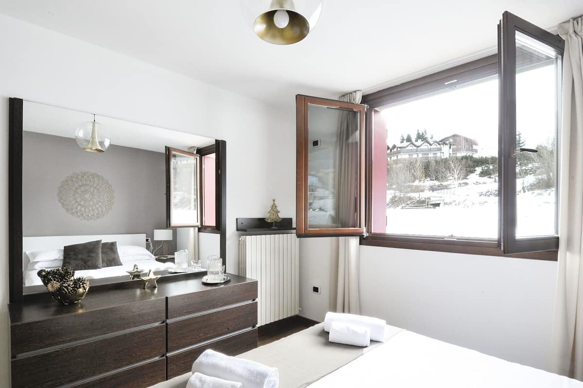 Een moderne hotelkamer met een groot bed, een dressoir, een spiegel en een raam met uitzicht op een besneeerd landschap.