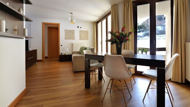 A modern interior with a dining area, wooden flooring, and large windows. - Residenze Holiday Park by Halldis (Ponte di Legno)