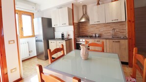 Eine moderne Küche mit Holzschränken, einem Edelstahlkühlschrank, einem Gasherd und einem Glastisch.