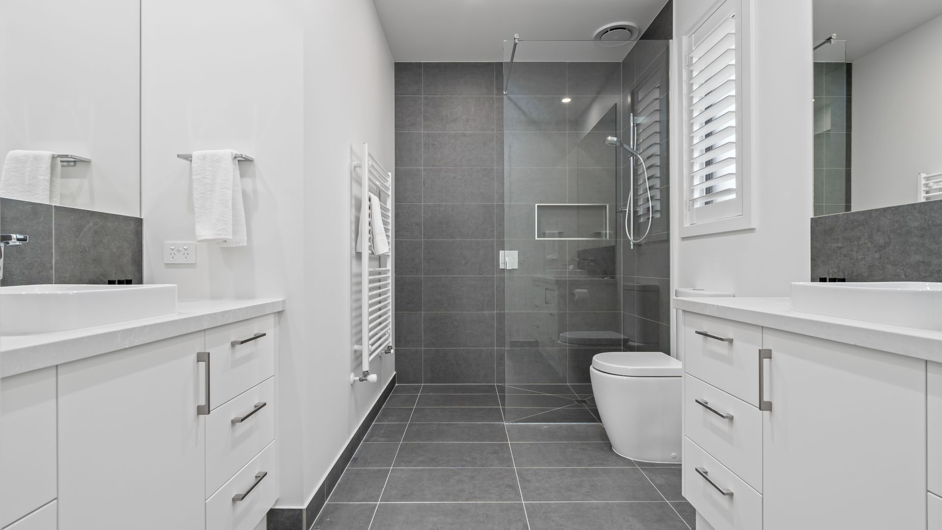 Ein modernes Badezimmer mit Dusche, Toilette und zwei Waschbecken.