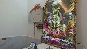 A room with a white table, a framed religious painting, and a white air conditioning unit on the wall. - Hotel Krishnam Palace (Vrindavan)