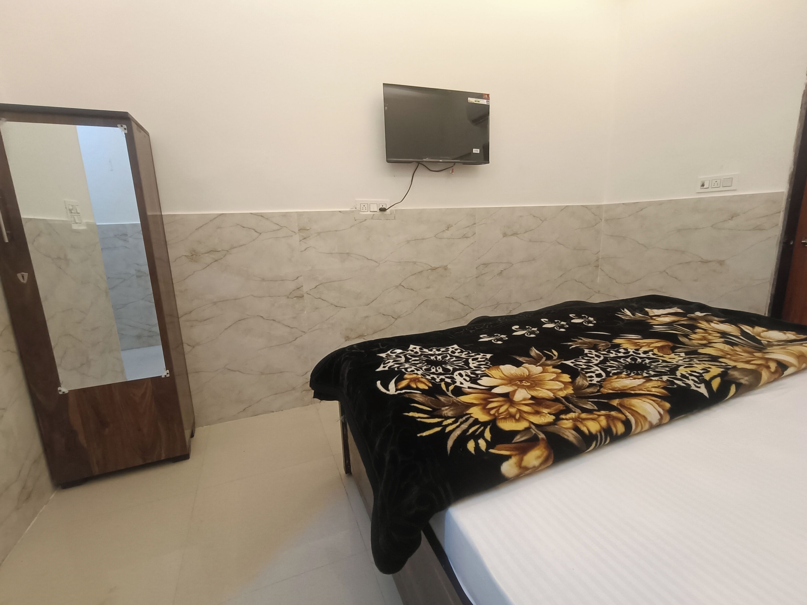 A bedroom with a bed, a wardrobe, a wall-mounted TV, and a power outlet.