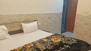 A hotel room with a bed, white pillows, a floral bedspread, and a marble-patterned headboard. - Hotel Krishnam Palace (Vrindavan)