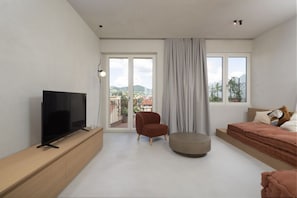 A modern bedroom with a TV on a wooden console, a red chair, a round ottoman, a bed with a pink blanket, and a city view through the window. - Modern Apartment with Skyline Views (Firenze)