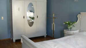 A bedroom with a white wardrobe, a bed, a small table with a vase, and a mirror. - Apartment 'Richard W, 90 sqm' in Weimar – up to 8 adults (Weimar)
