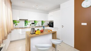 A modern kitchen with white cabinets, a wooden countertop, a blender, and a sink. - Family and child-friendly 5* villa with pool, games and fitness room (KORNIC)