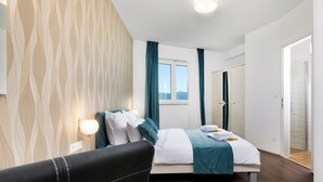 A modern hotel room with a bed, a bedside table, a chair, and a window with curtains. - Family and child-friendly 5* villa with pool, games and fitness room (KORNIC)