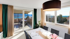A dining area with a table set for four, a large window with a view of the sea, and a balcony with outdoor seating. - Family and child-friendly 5* villa with pool, games and fitness room (KORNIC)