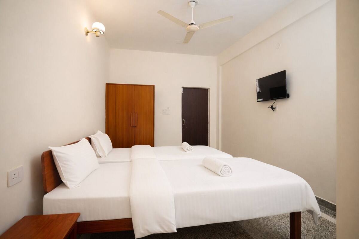 A hotel room with a bed, a wooden wardrobe, a ceiling fan, a TV, and a small wooden table.