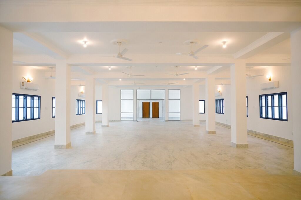 Un vestíbulo de hotel amplio, bien iluminado, con techos altos, ventanas grandes y una puerta central.