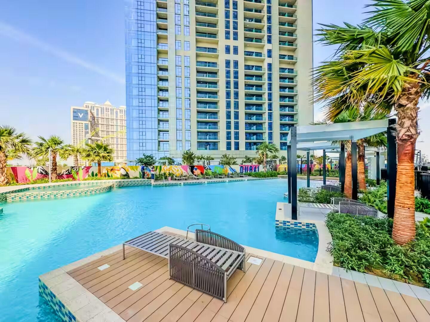 A swimming pool with a wooden deck, lounge chairs, and palm trees.