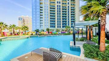 A swimming pool with a wooden deck, lounge chairs, and palm trees.