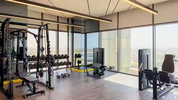 A modern gym with a variety of equipment, large windows, and a city view.
