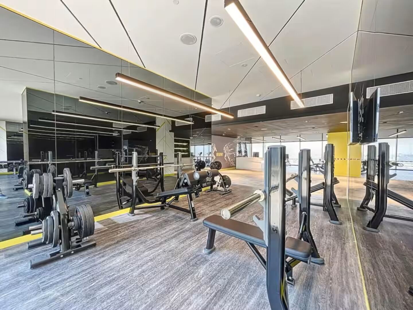 A modern gym with weightlifting equipment, mirrors, and a large window.