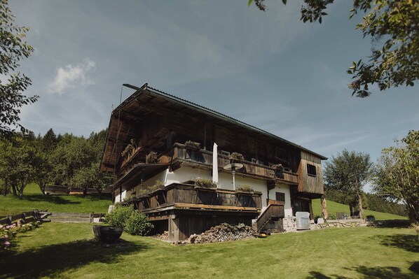 A traditional wooden chalet with a balcony, surrounded by a well-maintained lawn and trees.