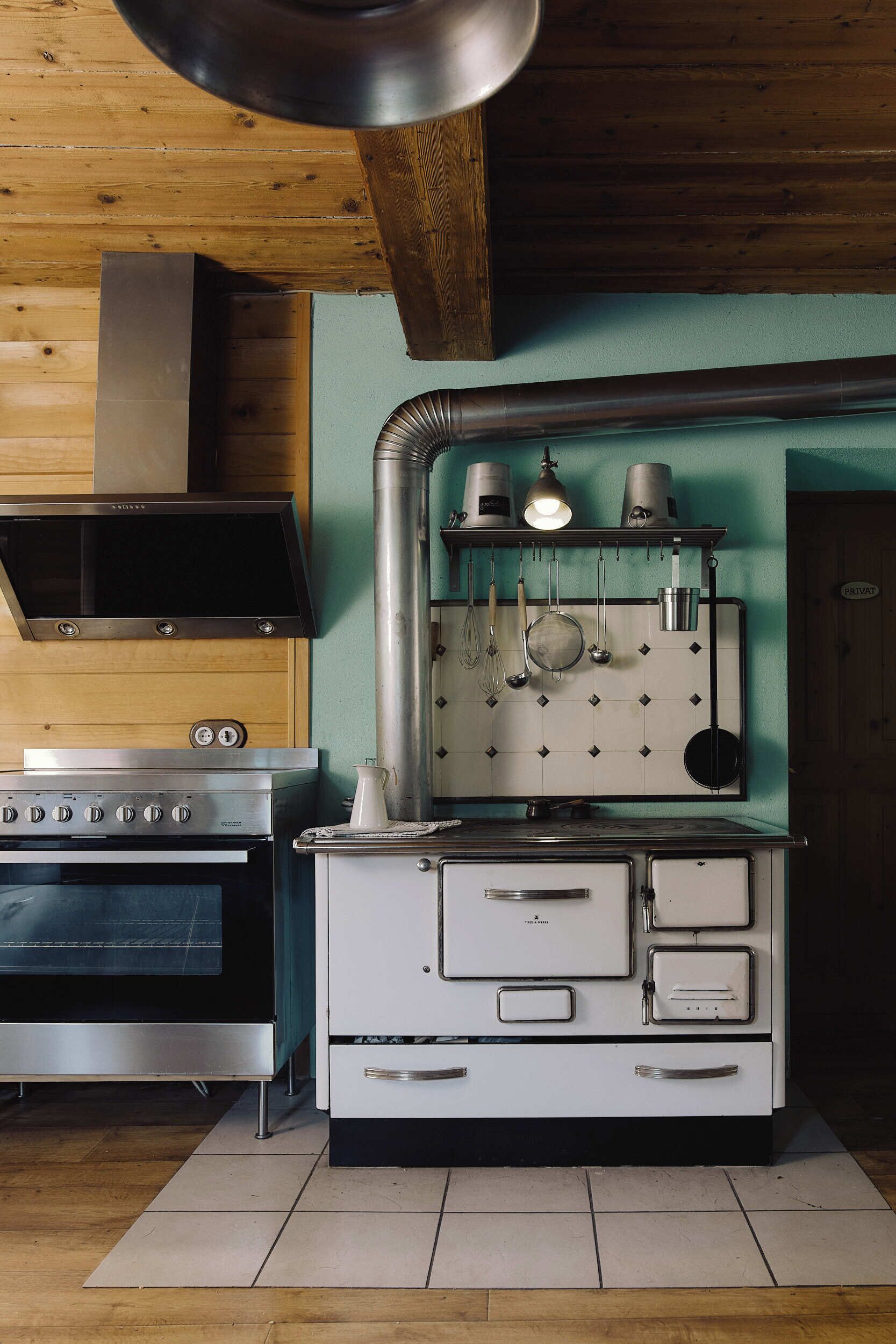 Une cuisine équipée d’une cuisinière en acier inoxydable, d’un four blanc et d’un porte-casseroles suspendu.