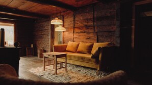 A cozy room with a wooden ceiling, a sofa with orange cushions, a wooden table, and a hanging light fixture. - Montenido - Rustic mountain farmhouse with infrared sauna and swimming pond (Oberau)