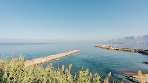 A coastal scene with clear water, a stone pier, and distant mountains.
