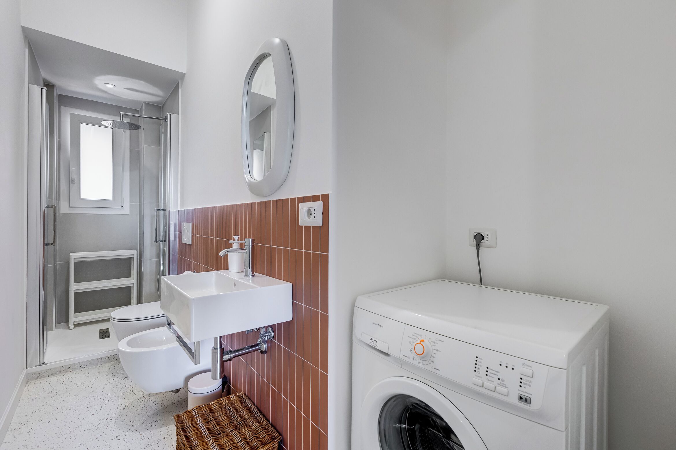 Un baño con inodoro, lavamanos, ducha y lavadora.