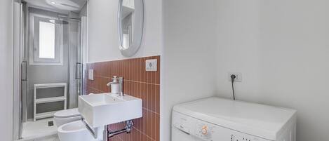 Un baño con inodoro, lavamanos, ducha y lavadora.