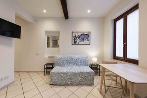 Un salon moderne comprenant un canapé, une table à manger, un téléviseur fixé au mur, une fenêtre et une œuvre d’art encadrée.