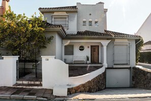 Ein zweistöckiges Haus mit Steineinfahrt, einer Holztür und einer kleinen Veranda mit einer Bank.