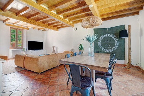 A modern living room with a wooden ceiling, a TV, a sofa, a dining table with chairs, and a decorative wall piece. - Casa Lounell: Pool, Spa, Sauna & Games Room in the Tarn Countryside (Graulhet)