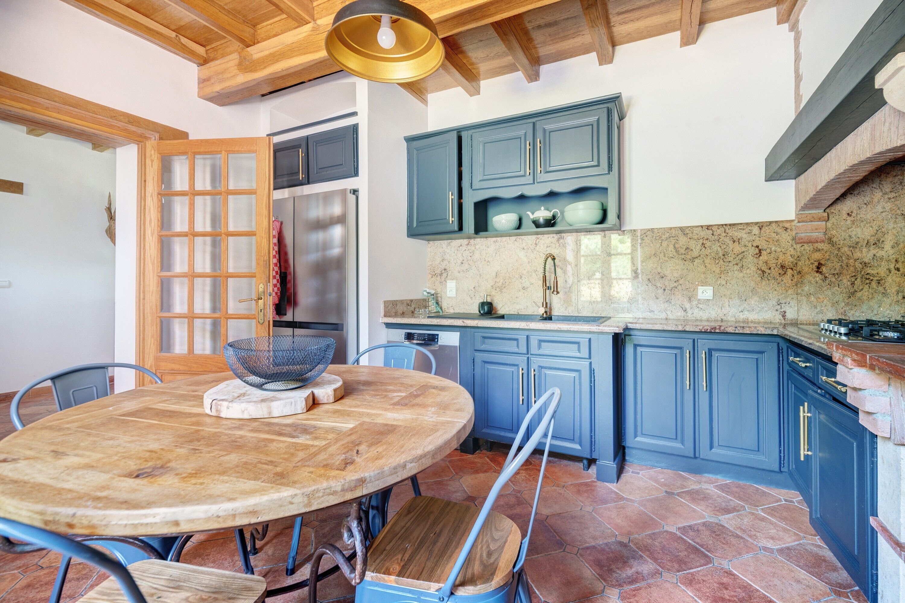 A kitchen with blue cabinets, a round wooden table, and a stone backsplash.