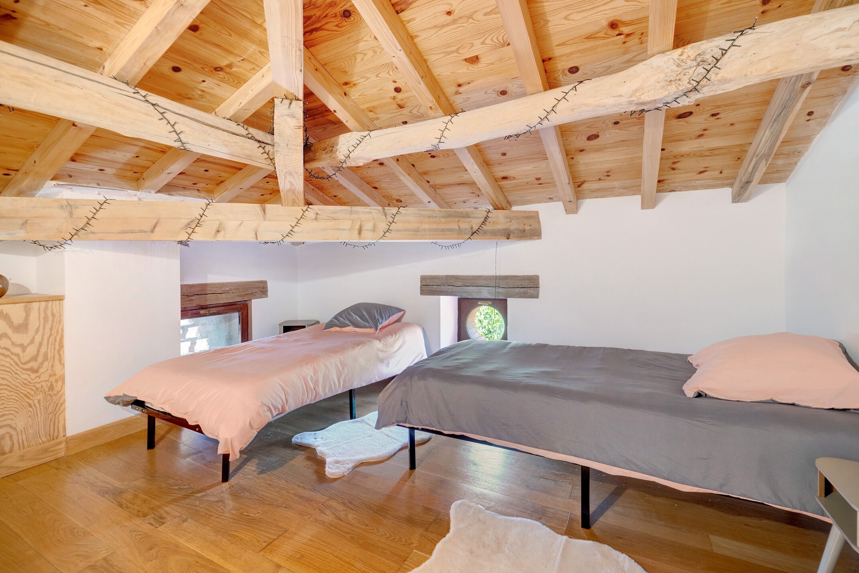 Ein Zimmer mit zwei Betten, Holzbalken an der Decke und einem Rundfenster.