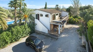 Ein zweistöckiges Haus mit Swimmingpool, einem geparkten Auto davor und einem Garten mit Palmen.