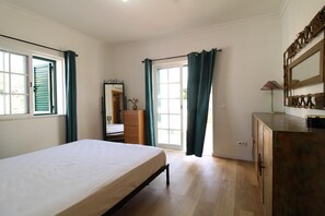 A bedroom with a bed, a dresser, a mirror, and a door leading to another room. - Villa GrandVale (Castro Marim)